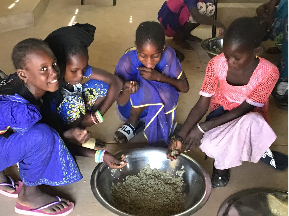 Four girls grab from a bowl of mung beans.